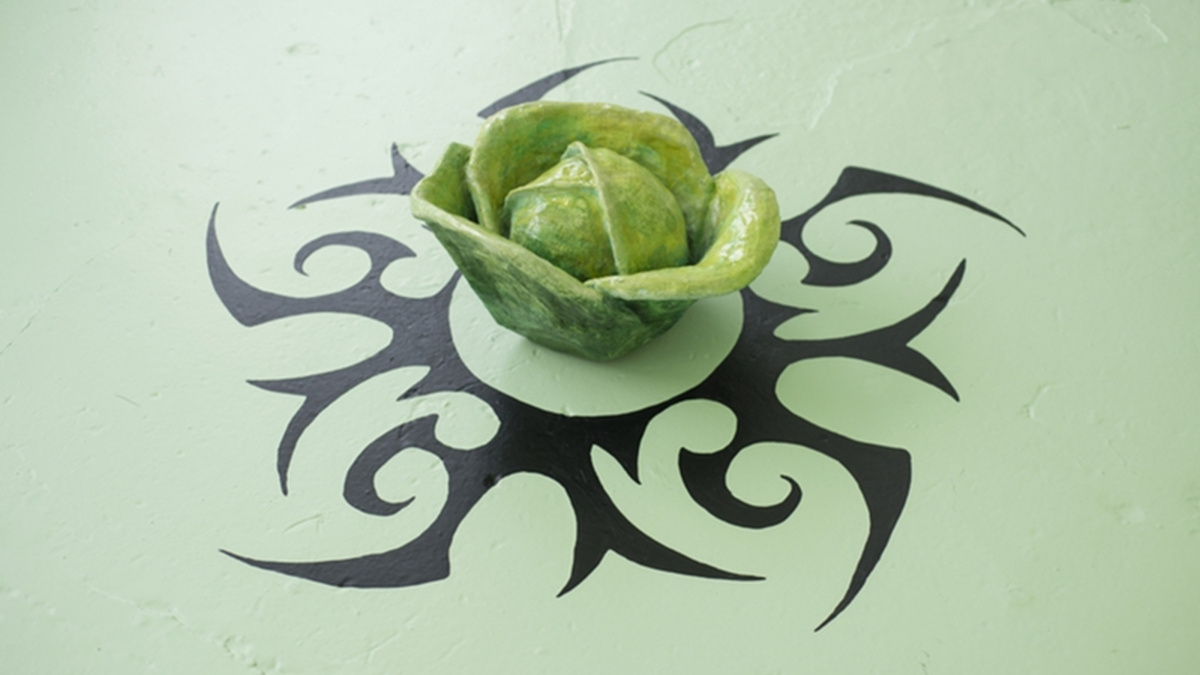 A small green sculpture of a rose sits on a green surface in the centre of a tribal pattern.
