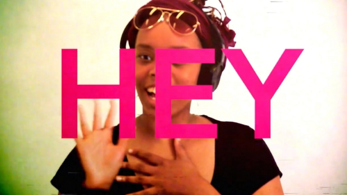 A person is shown from shoulders up waving at the camera. Superimposed across them in large pink text is the word HEY.