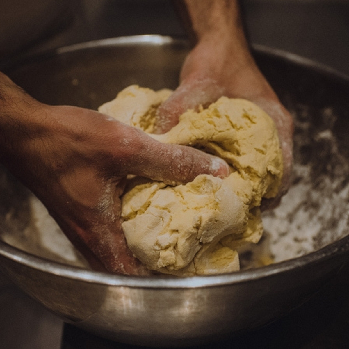 A pair of hands knead dough in a silver bowl.