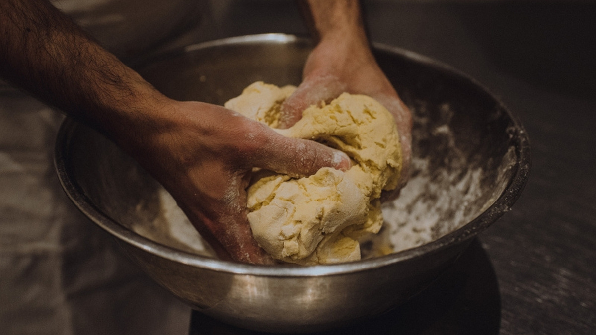 A pair of hands knead dough in a silver bowl.