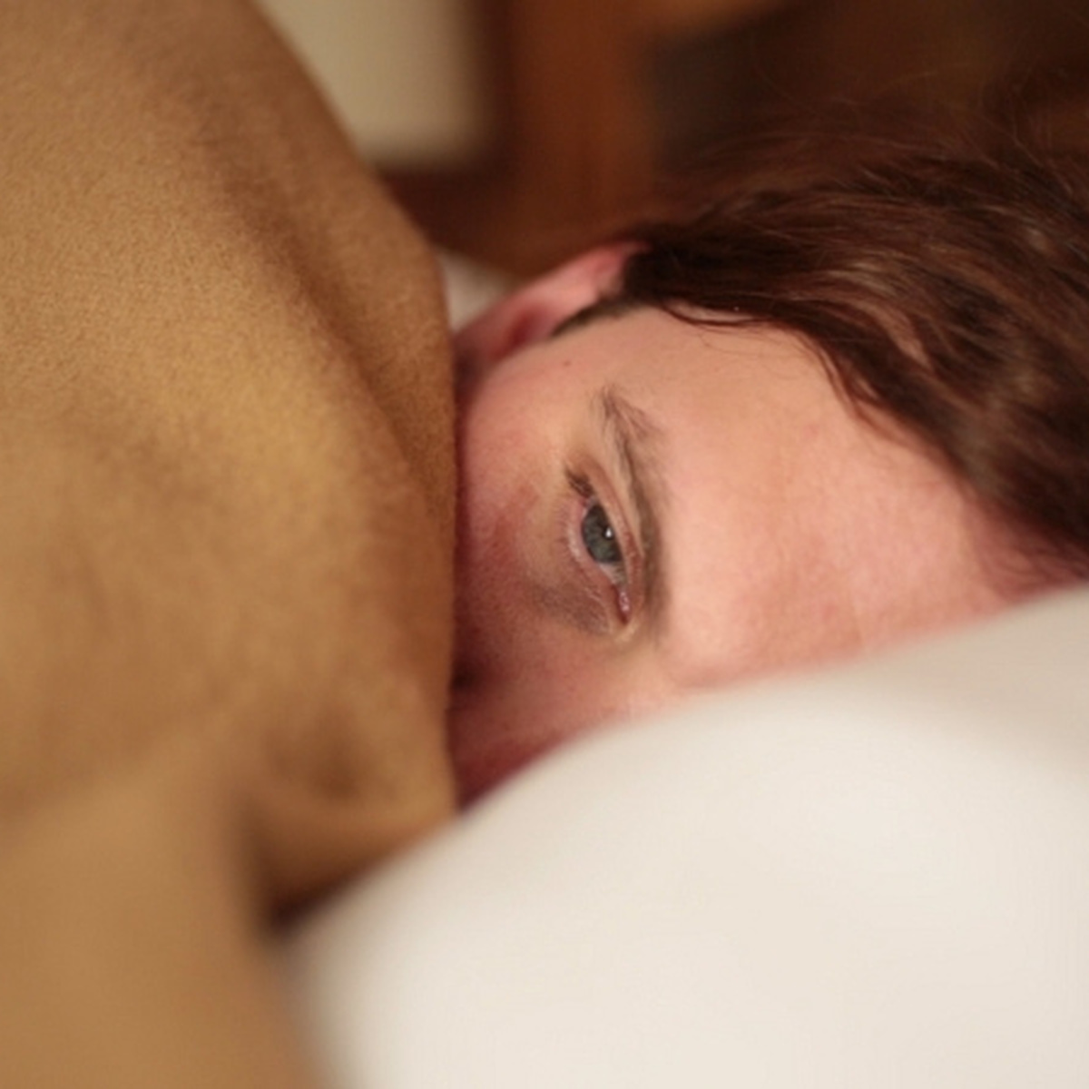 A person lies in bed, with a blanket half covering their face.