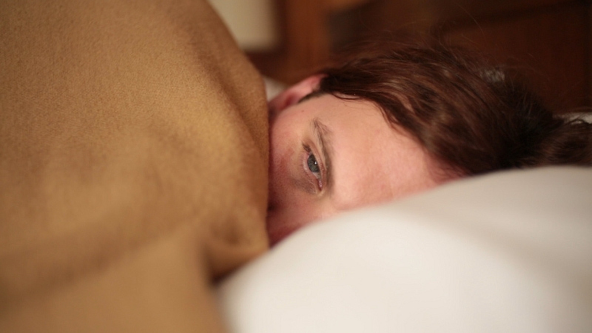 A person lies in bed, with a blanket half covering their face.