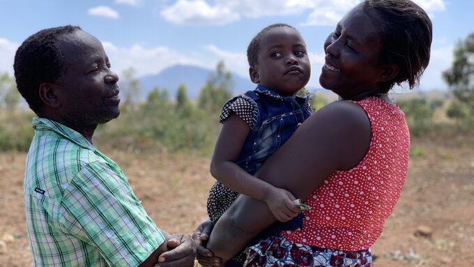 Outdoor shot of Anita, the film's Malawian protagonist, holding one of her children and smiling at her husband