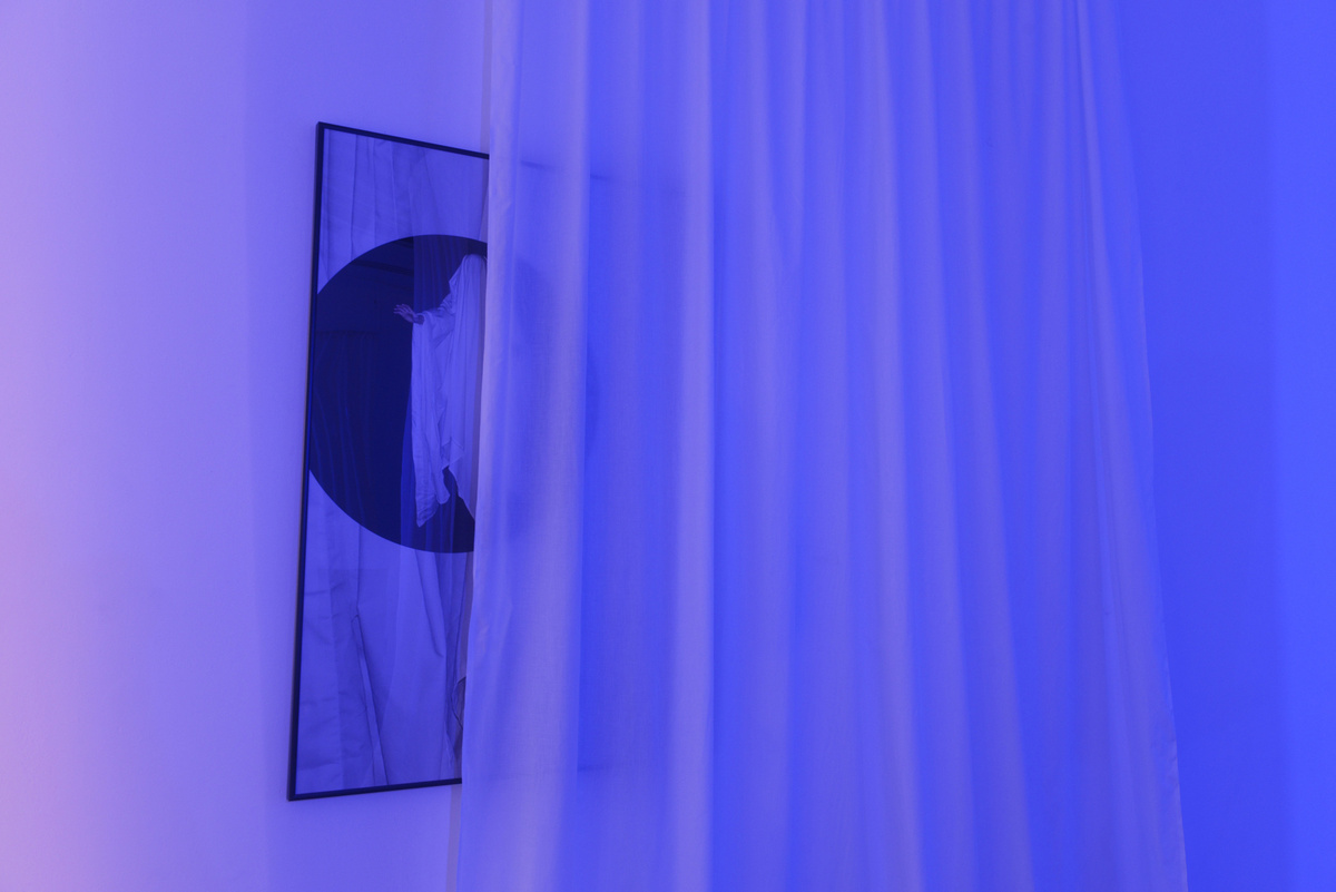 A thin white curtain hangs over an image of a ghost, all lit with a bright blue light.