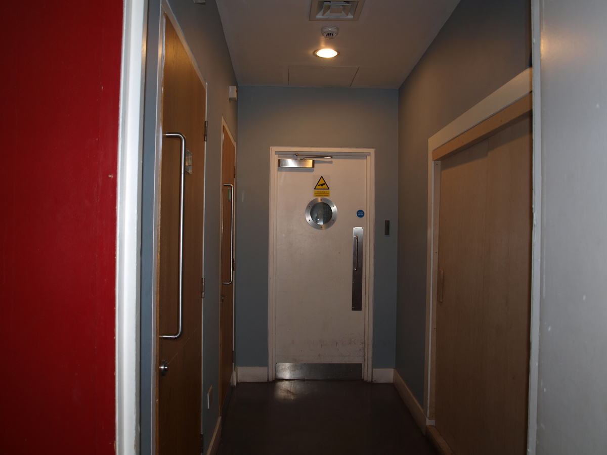 A photograph of a corridor. A white door with a circular window is at the end of the corridor.