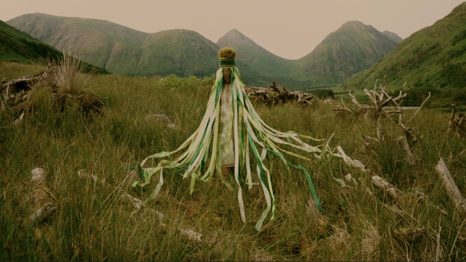 A costumed folkloric femme figure stands in the Glen Etive Forest’s rewilding project in embroidered ankle-length blouse
