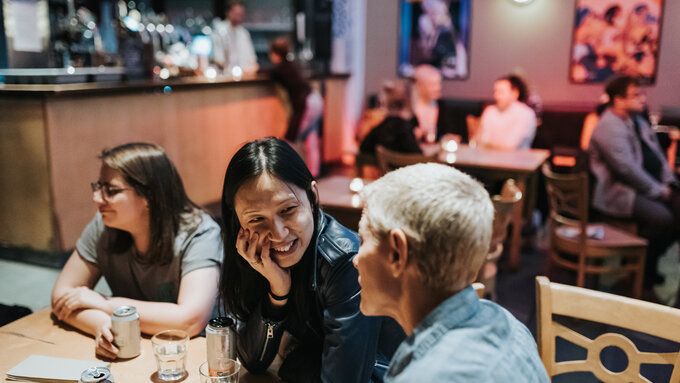 Three people sitting at a table in the CCA bar, with mellow lighting. The mood is friendly and social.