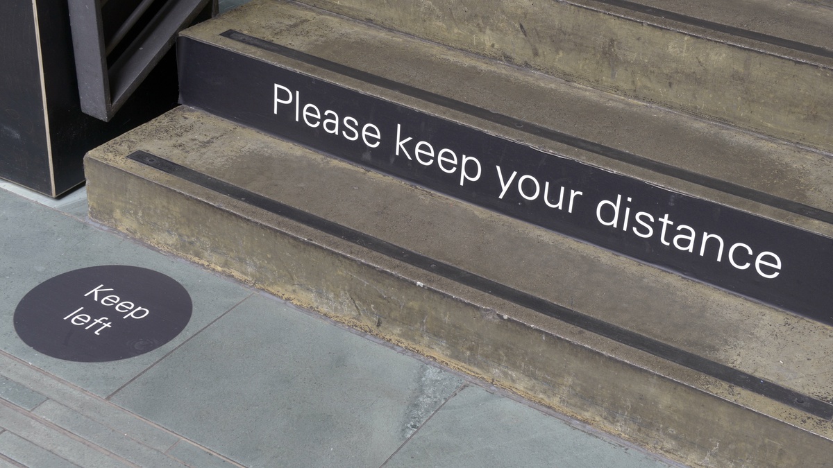 A photograph of the bottom of a stairwell, the text "Please keep your distance" is printed on the stairs.