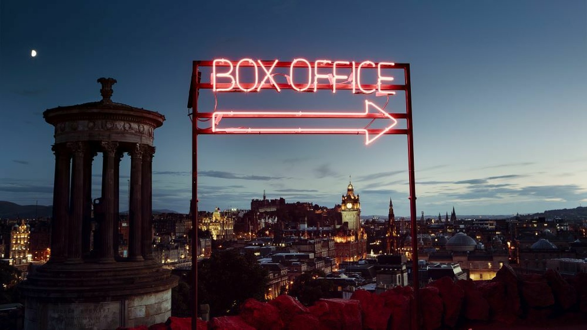 A backdrop of Edinburgh at night. In the foreground is a red neon sign that says "Box Office"