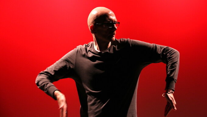 Older man dancing against a red backdrop.