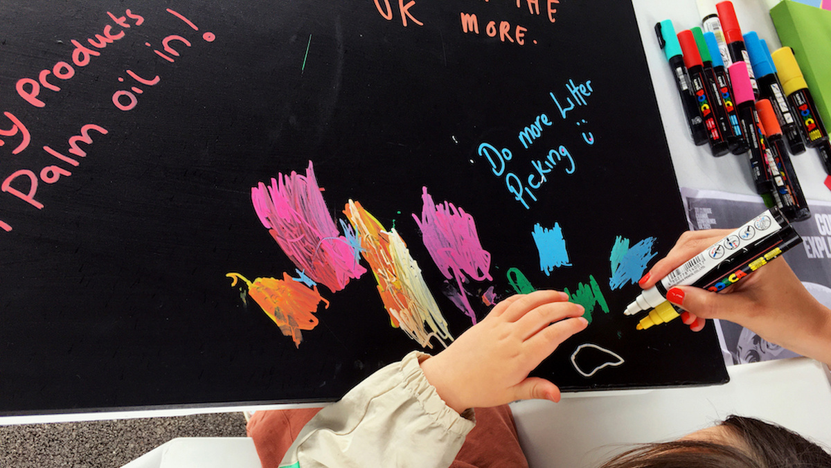 Black chalkboard with scribbled pen markings in orange, pink and blue. Some handwriting reads 'Do more litter picking'.