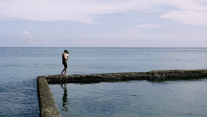 A person walks along a concrete path in the sea, holding a baby.