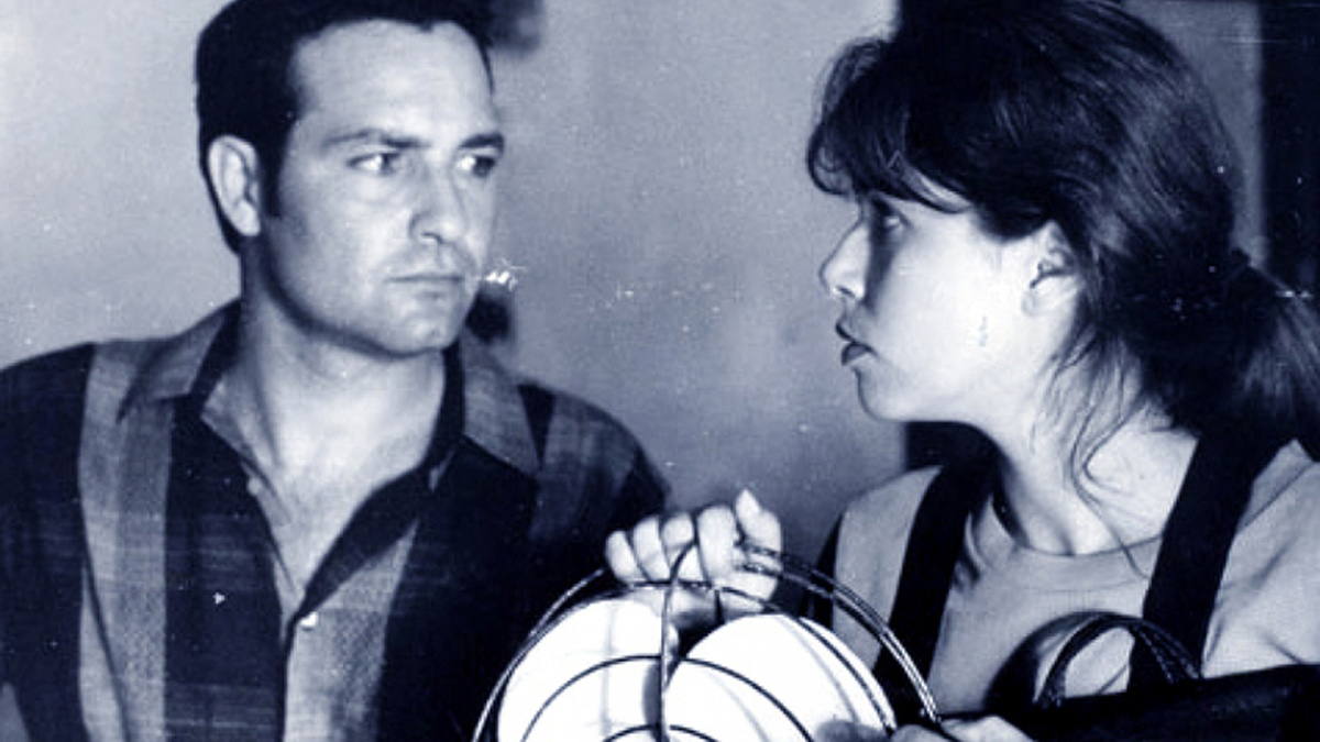A black and white image of a man staring at a woman who is holding an old fashioned fan and staring back at him.