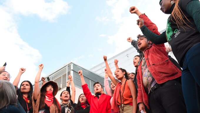 Diverse group of people holding up fist to a blue sky.