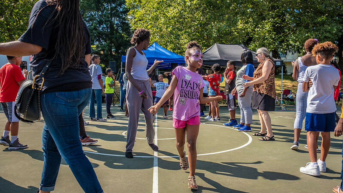 Community festival on basketball ground with women and children. Central focus on one girl jumping