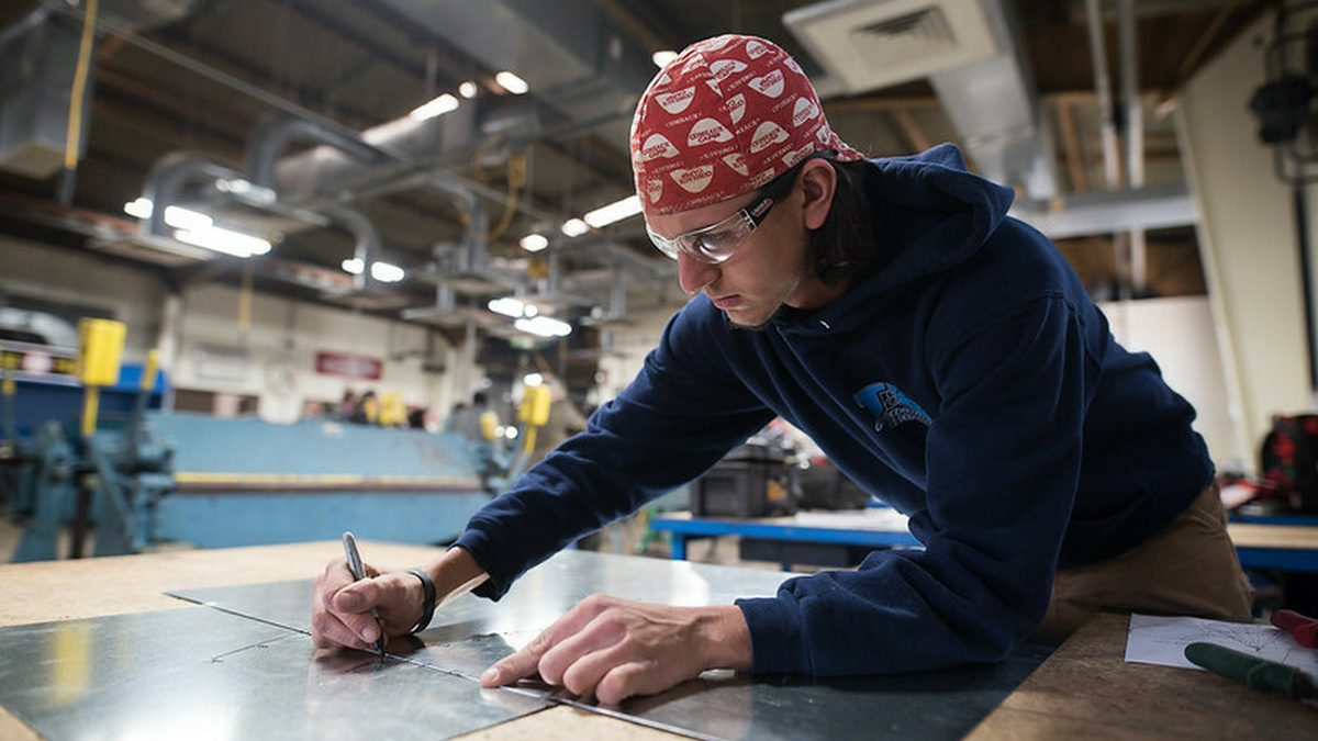 Worker drawing on metal sheet in factory.