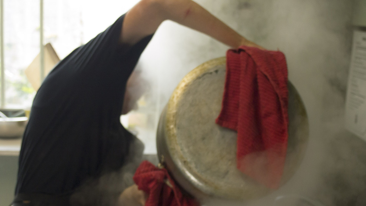 Person holding a cooking pot in steam.