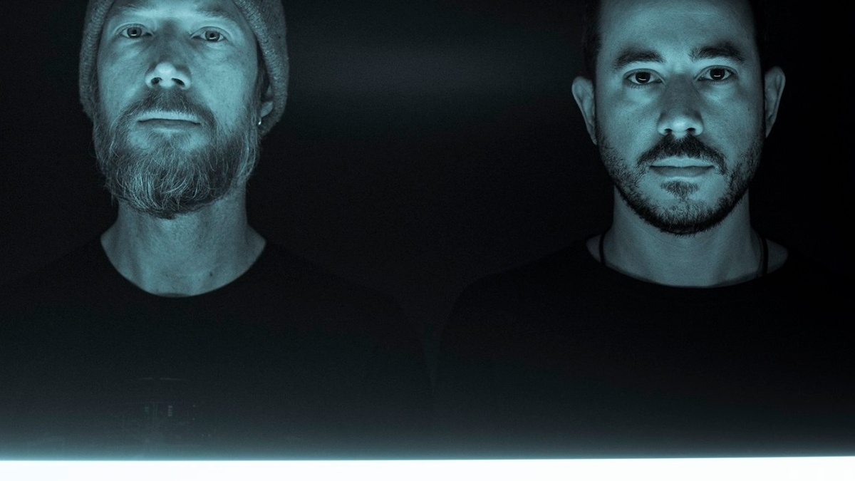 An image of two people with beards standing behind a fluorescent light.