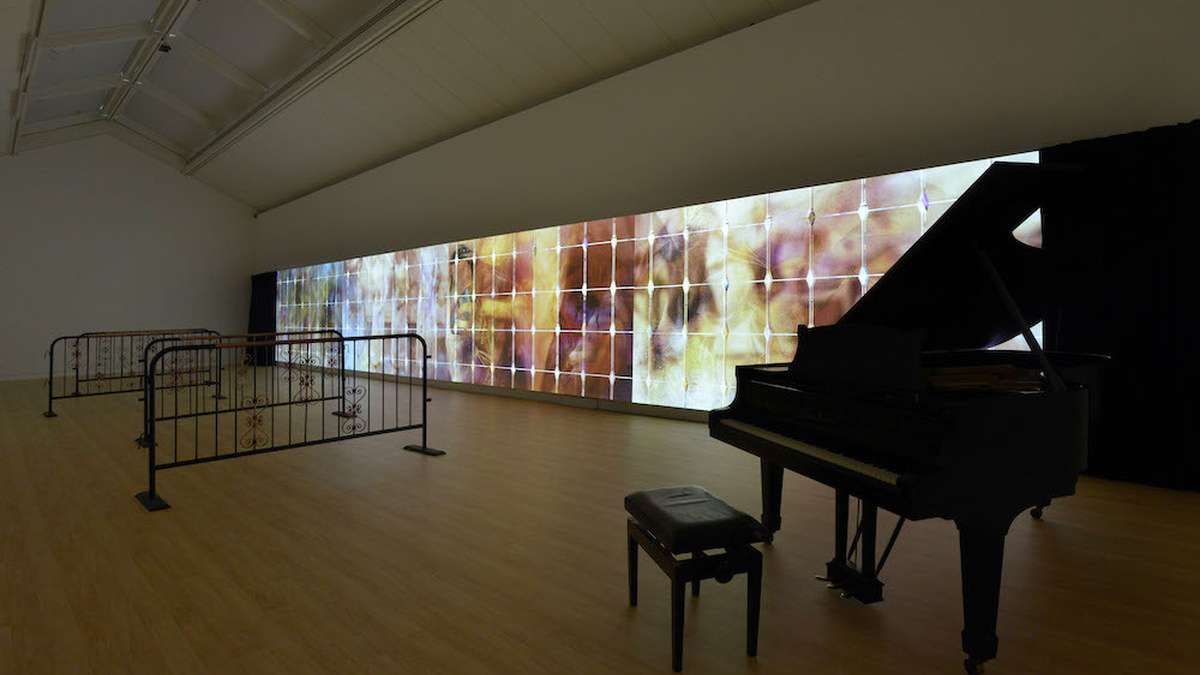 A gallery space with a colourful projection on one wall. There is a grand piano within the space.