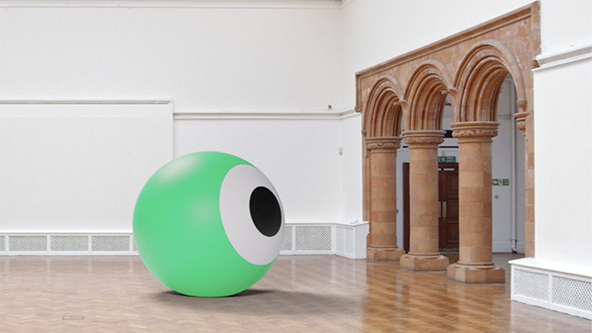 A white gallery space with older stone arches, in the room there is a large green sphere that looks like an eye.