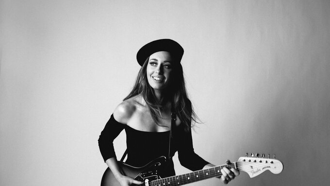 In black and white, a young woman holds an electric guitar.