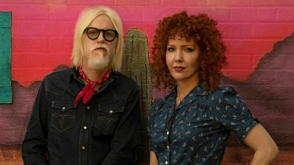 A man and a woman, he is wearing large glasses and a bandana tied around his neck, she has curly red hair.