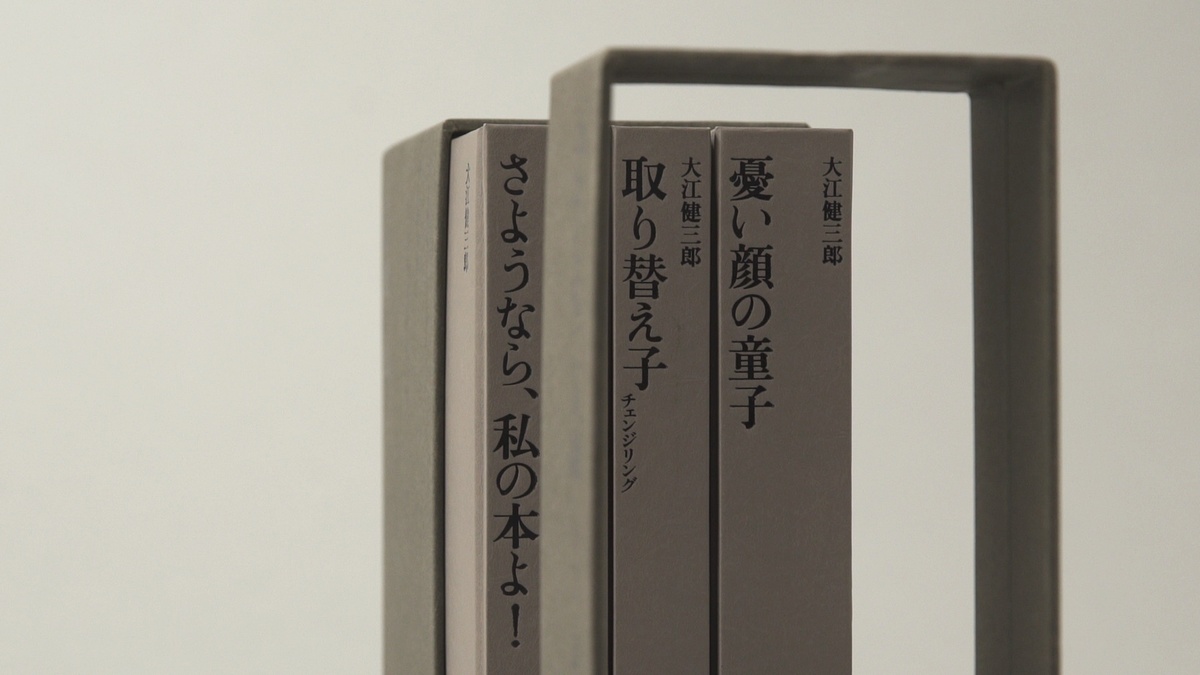 Three book spines in a box with lid positioned in foreground, against a grey background.