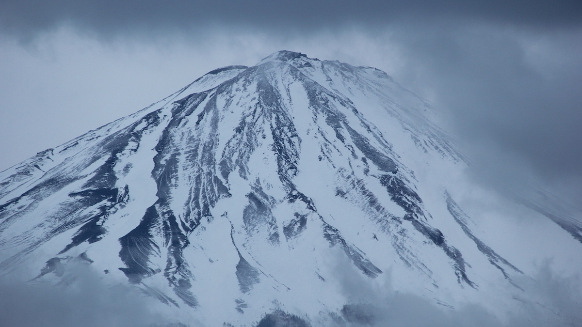 The peak of Mount Fuji covered in snow and surrounded by clouds.