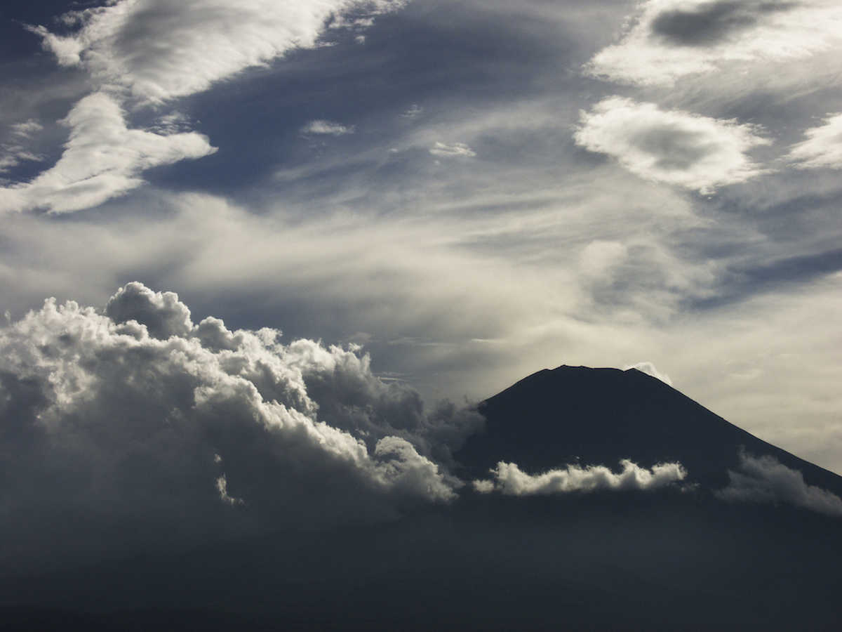 Silhouette of Mount Fuji surrounded by white clouds against a blue sky