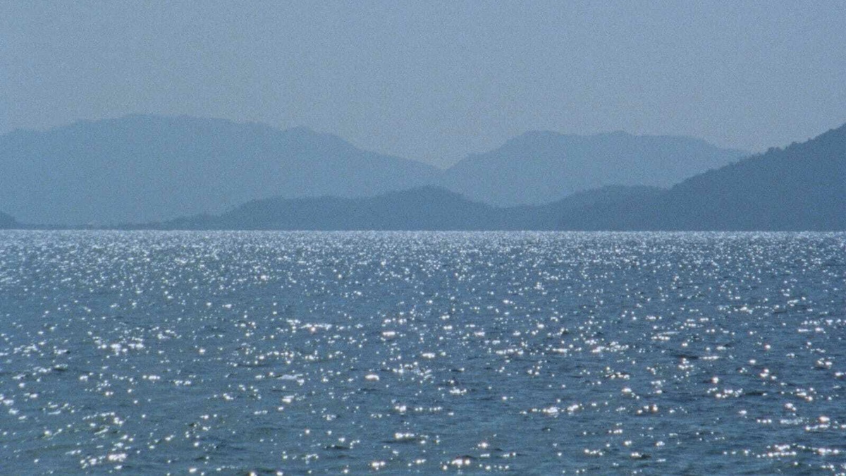 Sparkling blue sea water with silhouettes of mountains in the background.
