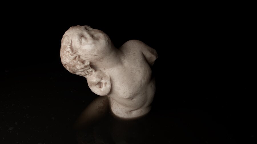 A small marble statue with a flaw in its face against a black background.
