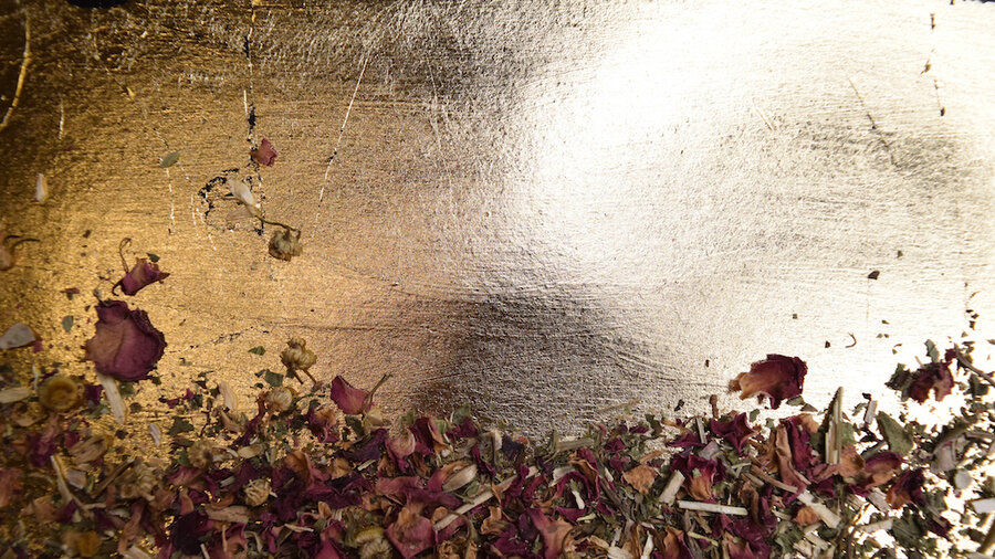 Dried rose petals and dried chamomile strewn on backdrop of shining gold leaf.