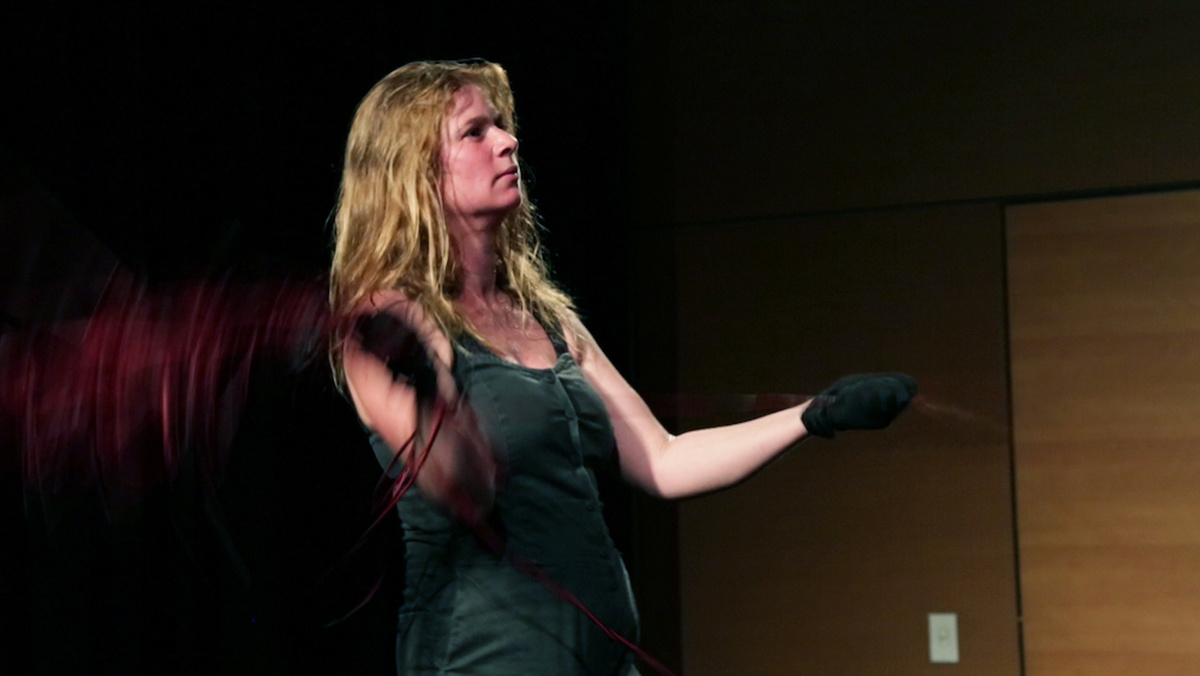 A woman onstage twirling microphones at the end of long cables causing the image to blur.