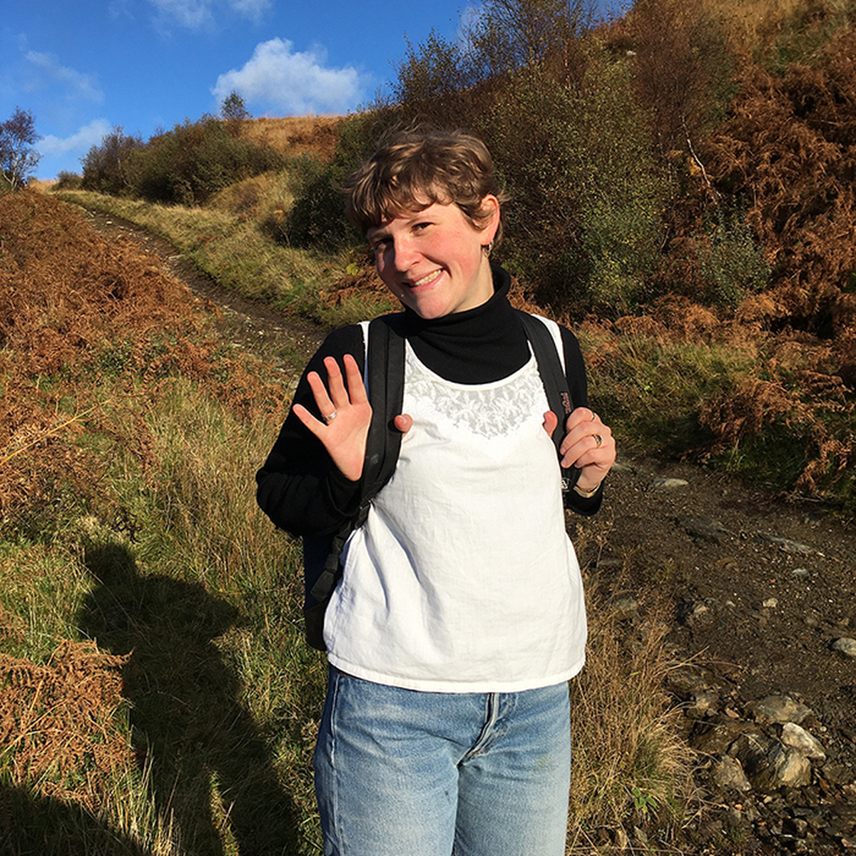 Anna Vlassova smile and waves at the camera in a rugged moorland setting.