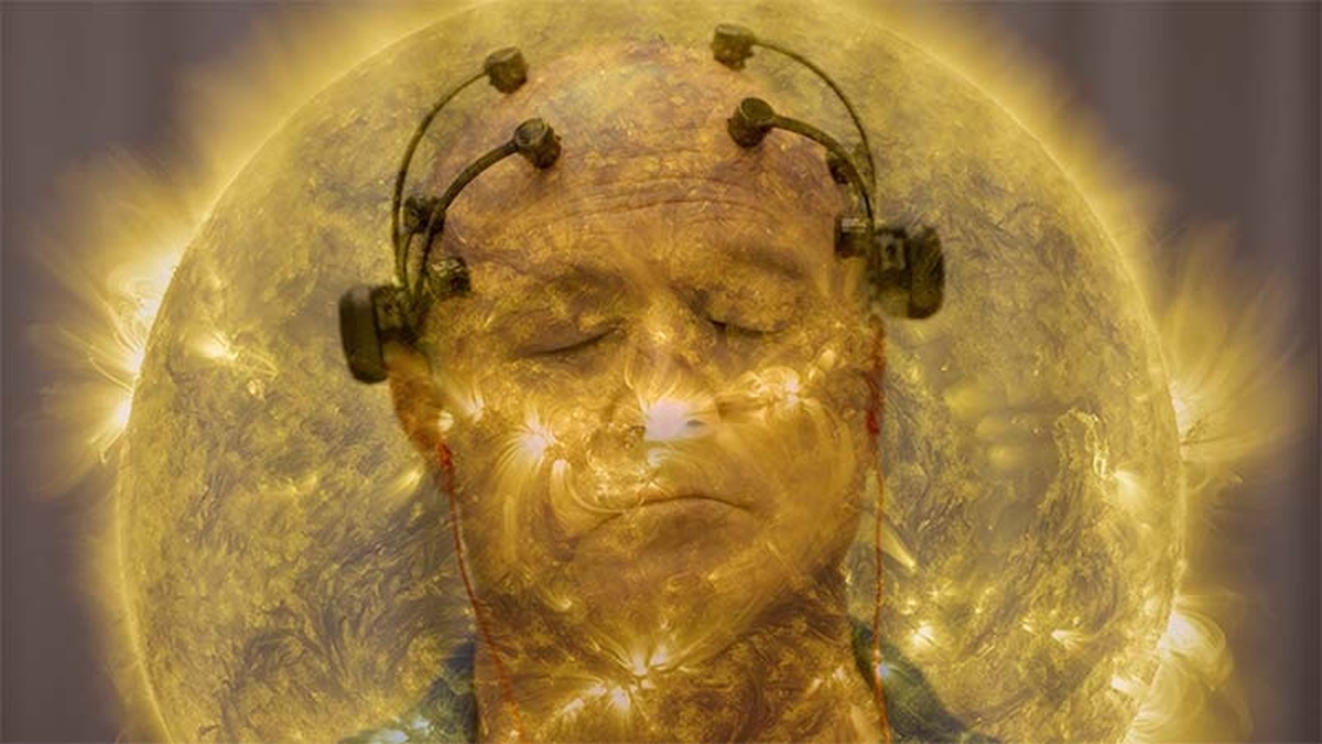 A person's head, wearing brain monitoring headset and earphones, superimposed over the surface of the sun.