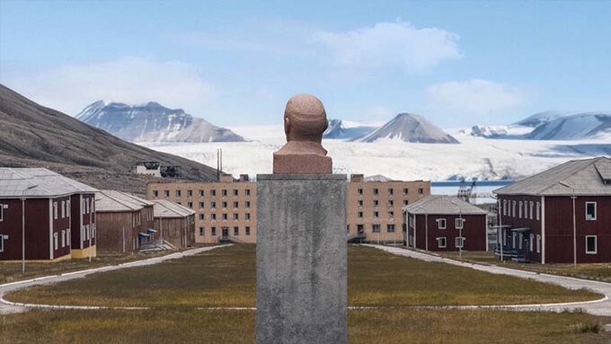 A stone bust sits on a plinth, overlooking a grass pitch, cluster of institutional buildings and snowy mountain range.