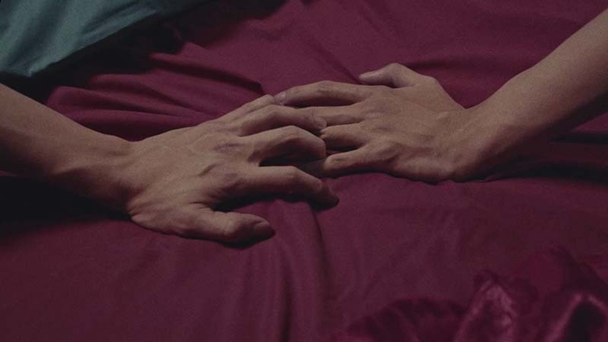 Two hands reach across red fabric, their fingers gently touch.