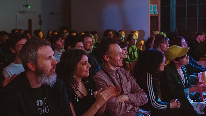 An audience sitting in a room clapping their hands.