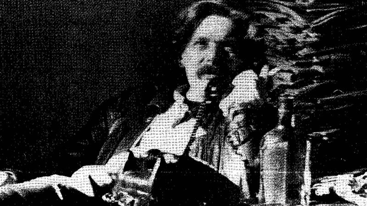 A black and white, grainy image of a man reclining on an armchair, holding a corded telephone to his ear.