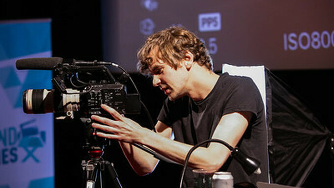 A young filmmaker looks through the lens of the camera, concentrating intently.