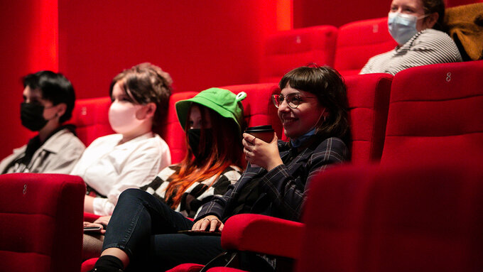 Four people sit in a row of cinema seats listening.