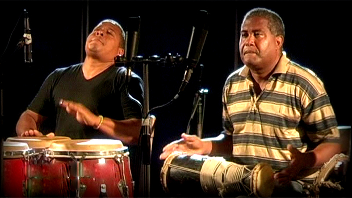 Two people playing percussion instruments sitting down with microphones.