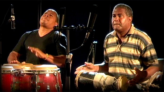 Two people playing percussion instruments sitting down with microphones.
