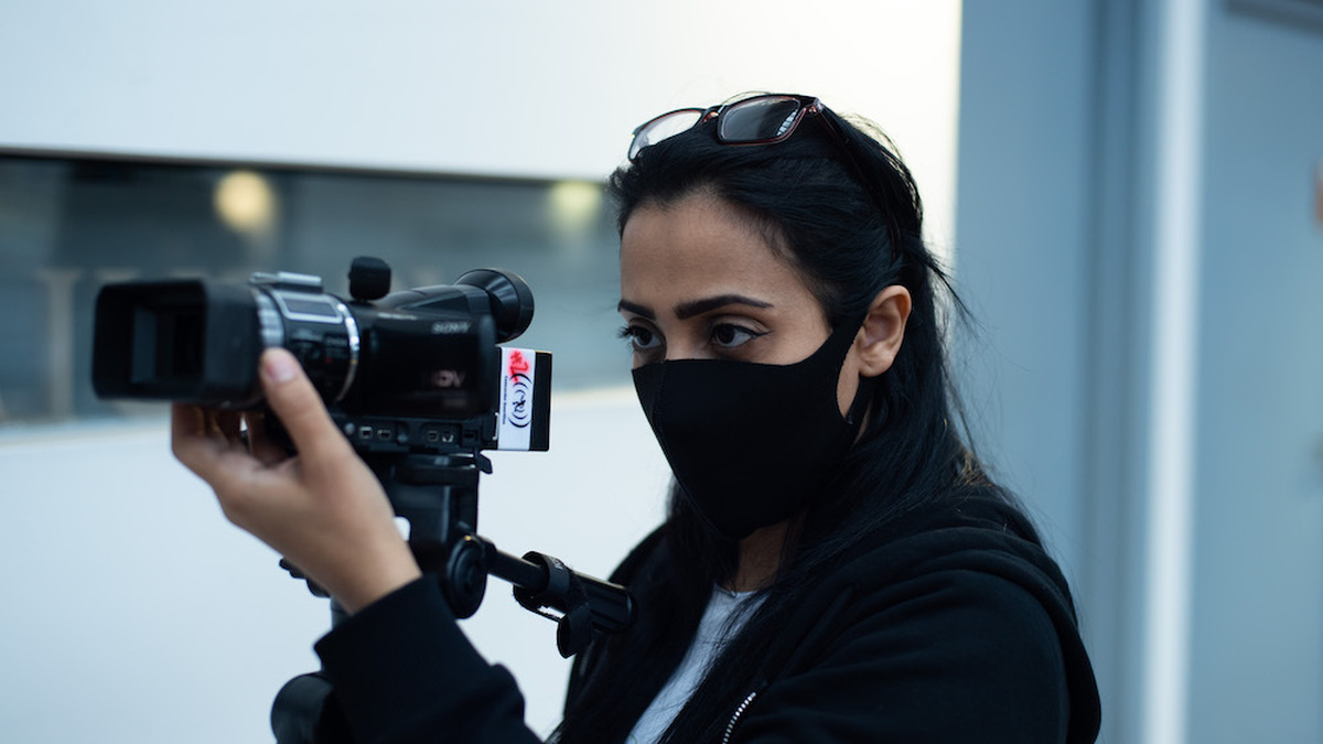 A person wearing a face mask and pointing a camera.