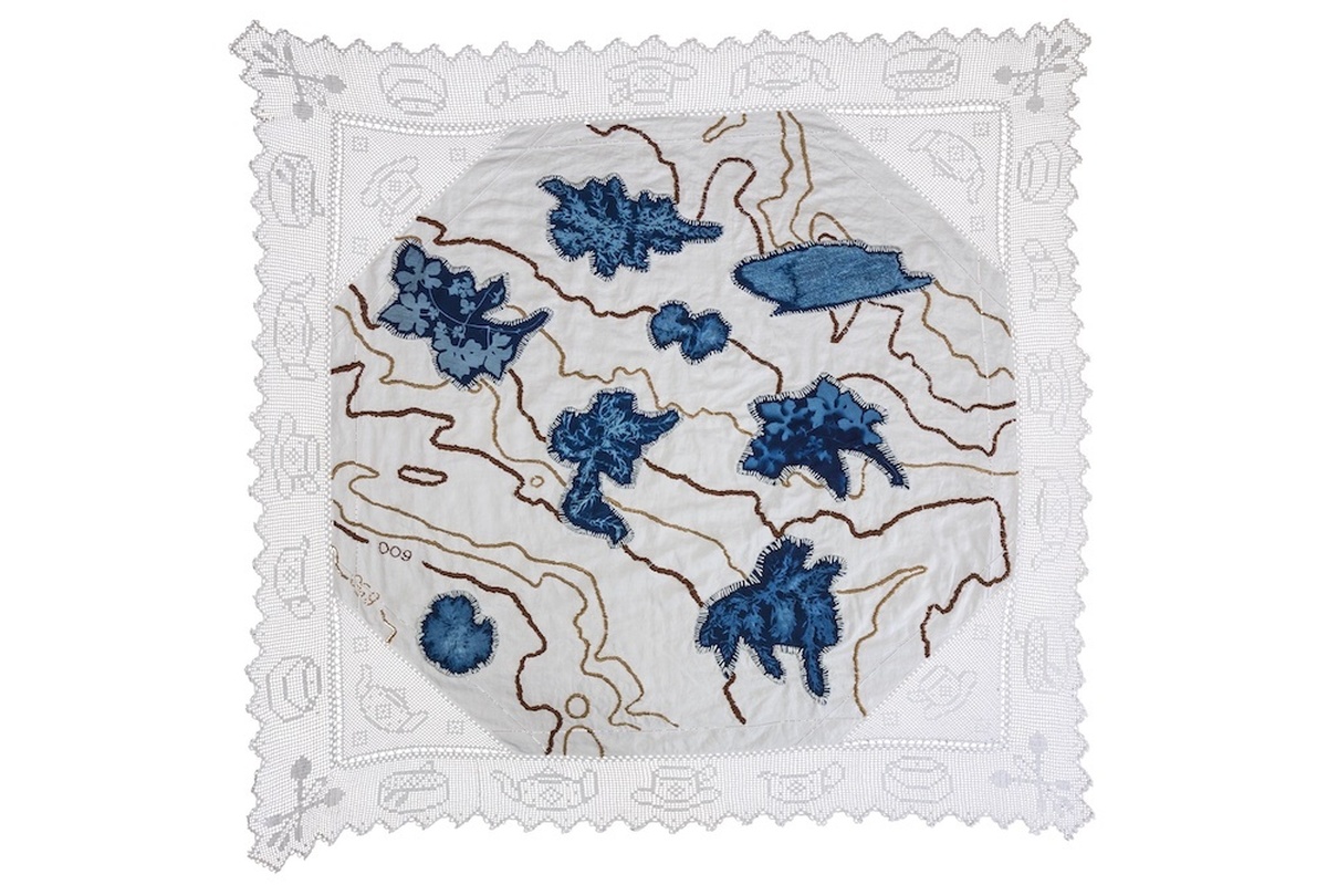 A rectangle of embroidered fabric with what looks like a map with the locations of various plants in the middle.
