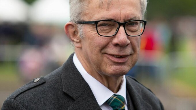 A man wearing glasses and a kilt jacket is pictured outside at an outdoor event.