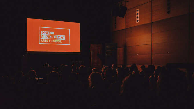 Audience in a cinema watching a screen with the Scottish Mental Health Arts Festival logo on it.