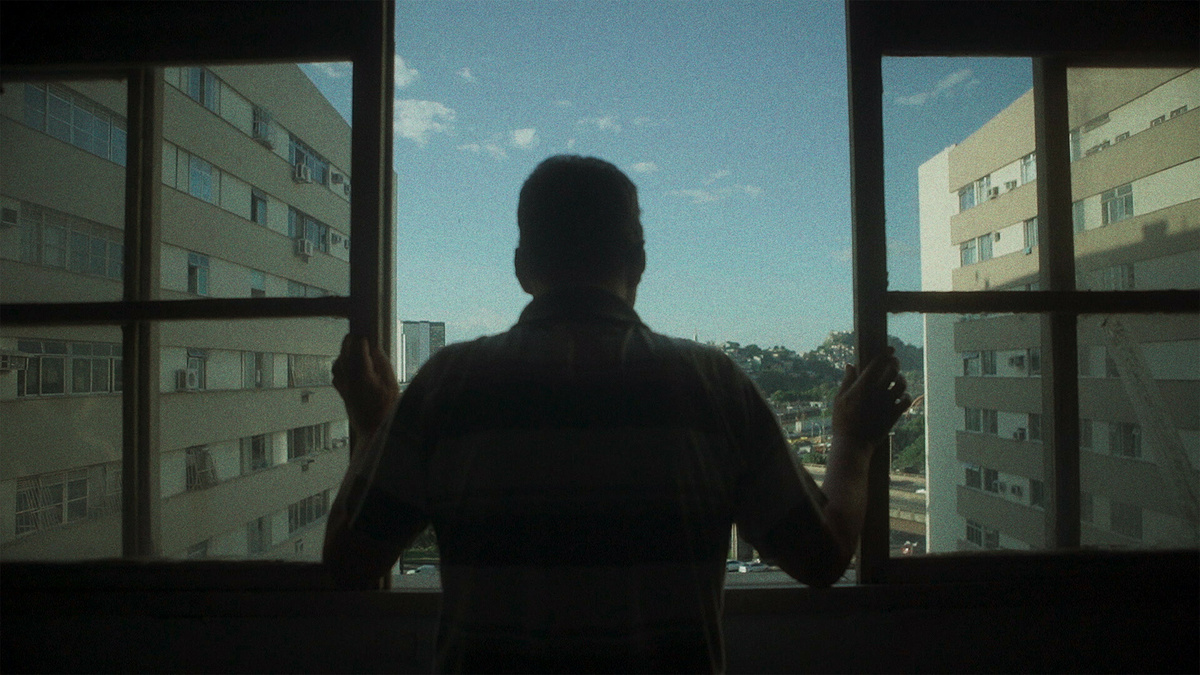 A person stands looking at their open window in a block of high flats on a sunny day.