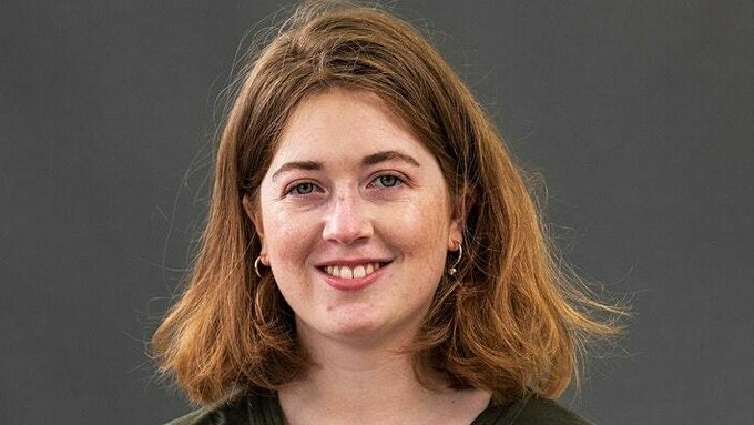Fiona Mozley smiling with a dark green top and grey background behind her.