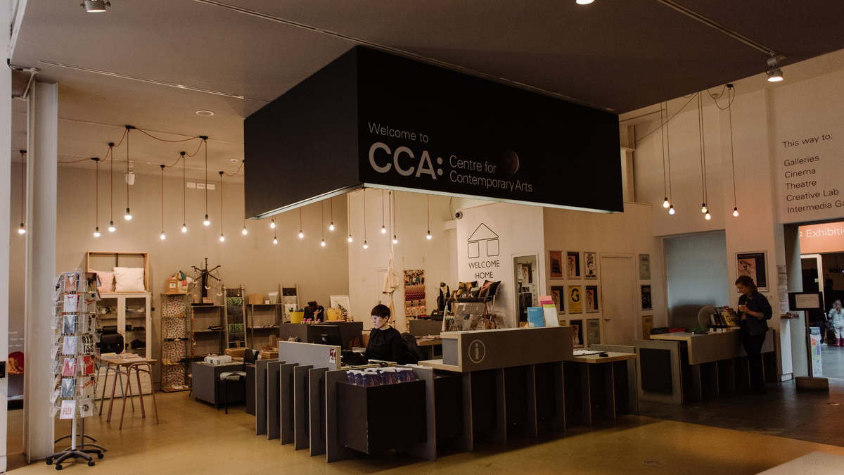 A cosy photo of CCA's foyer space, showing the box office with attendant and a shop area with cards and crafts.